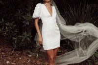 04 a modern plain mini wedding dress with a deep neckline, puff sleeves, white mules, pearl earrings and a long veil for a retro-inspired look