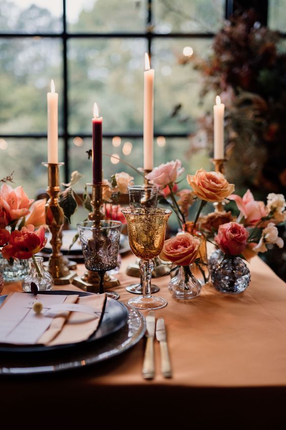 a bright wedding tablescape with blush, peachy and coral blooms, a rust-colored tablecloth and napkin, tall and thin candles