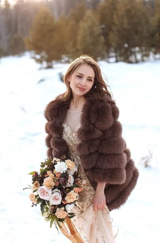a glam gold embellished wedding dress paired with a brown faux fur jacket with short sleeves for a super glam winter bridal look