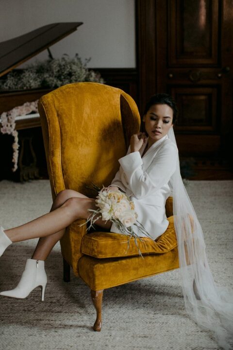 a modern bridal look with a white blazer wedding dress, white booties and a long veil is inspired by the 70s and boho style