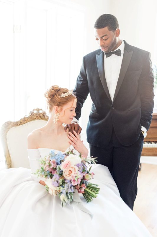the bride and the groom wearing Bridgerton-inspired looks - a black tux and an off the shoulder wedding ballgown with a gorgeous tiara and statement earrings