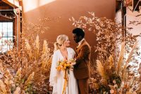 09 an earthy-toned floral wedding altar with blooms, grasses and dried leaves, a rust-colored backdrop is amazing