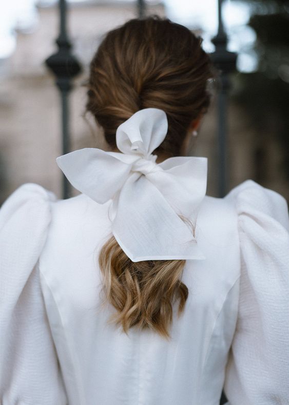 a modern refined wedding look with a red with puff sleeves, a low braid accented with a white bow is a gorgeous idea