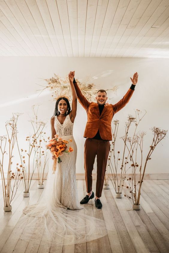 an earthy wedding altar of dried blooms and branches, a groom wearing a pretty rust-colored suit and a bride carrying a rust-colored bouquet