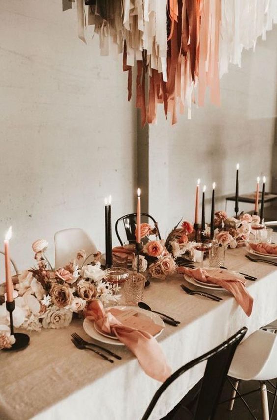 a beautiful earthy-tone wedding tablescape with neutral, rust, coral and orange blooms, copper napkins and candles and matching fabric strips over the table