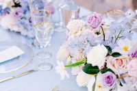11 a beautiful periwinkle wedding tablescape with a peri tablecloth, peri, peachy and lilac blooms, pillar candles and gold-rimmed glasses