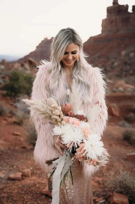 a light pink fuzzy fur coat over a rose gold sequin sheath wedding dress for a bold and edgy boho wedding look