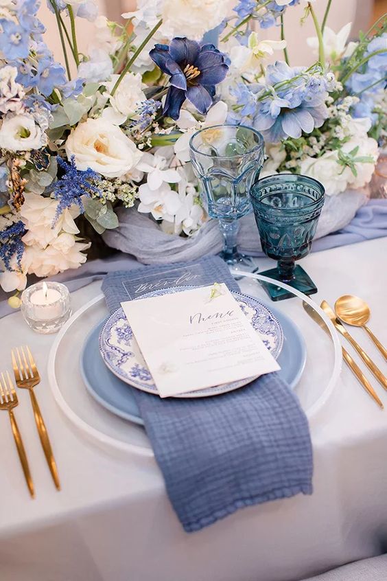 a beautiful tablescape with a periwinkle table runner, napkin and a plate, with a lush floral centerpiece of neutral and periwinkle flowers