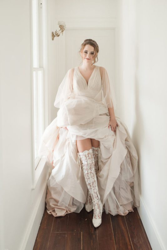 a jaw-dropping bridal look with an A-line wedding dress with a draped bodice, semi sheer puff sleeves and over the knee lace boots