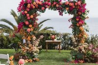 13 a super colorful wedding arch with tropical leaves, pink, orange, yellow and neutral blooms all over for a tropical wedding