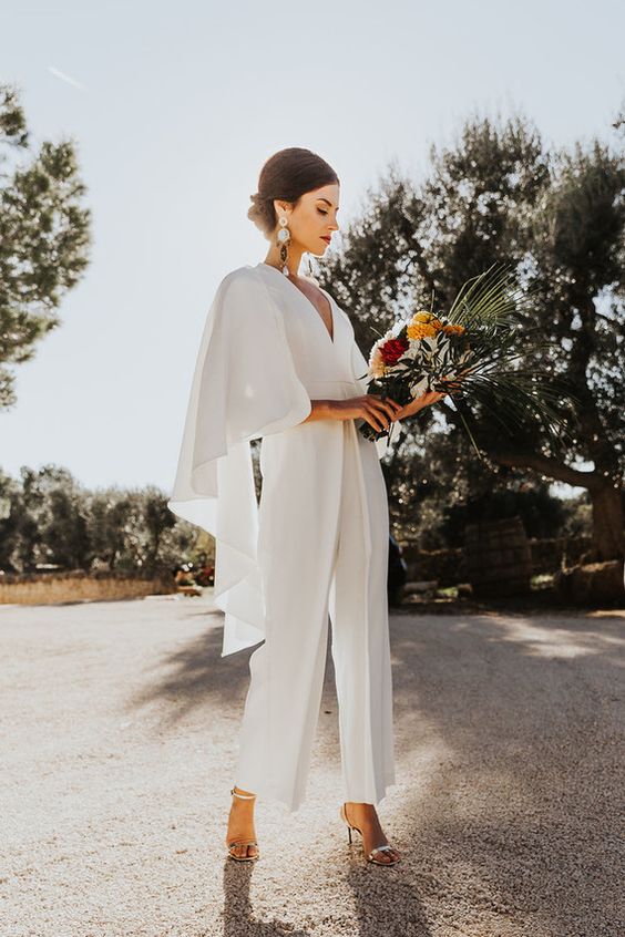 a chic plain white jumpsuit with a capelet and a deep V-neckline, silver shoes and statement earrings for a bold look