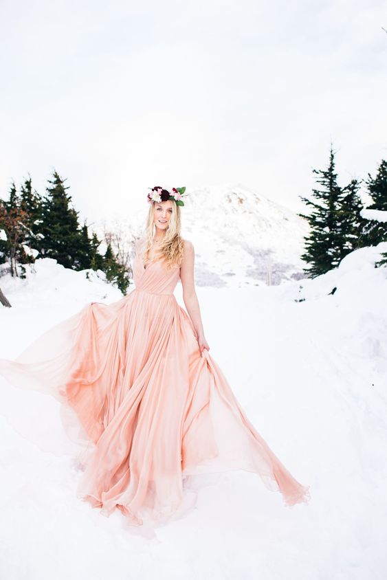 a pink strapless A-line wedding dress with a draped bodice and a pleated skirt with a train plus a bold floral crown for a winter bride