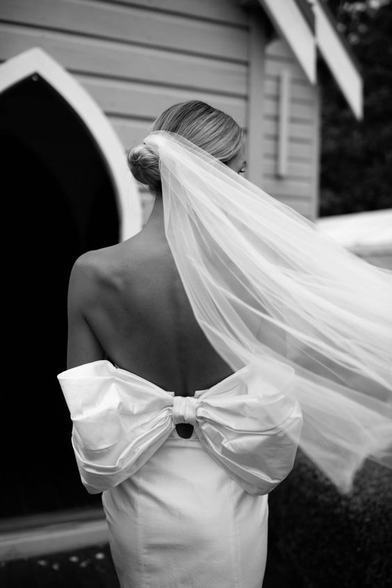 an adorable fitting wedding dress with an open back and a large bow plus a long veil for a dreamy and very romantic wedding look