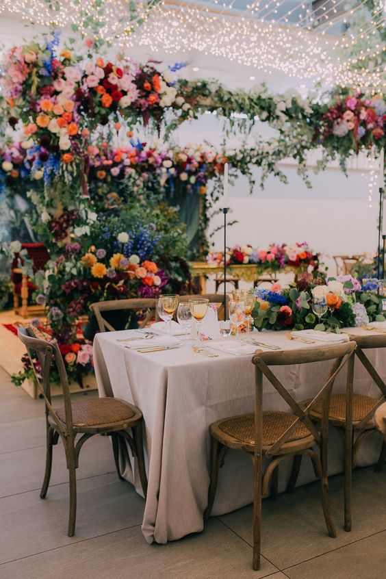 a gorgeous colorful wedding reception space with greenery and super bold blooms all over the space and string lights over it
