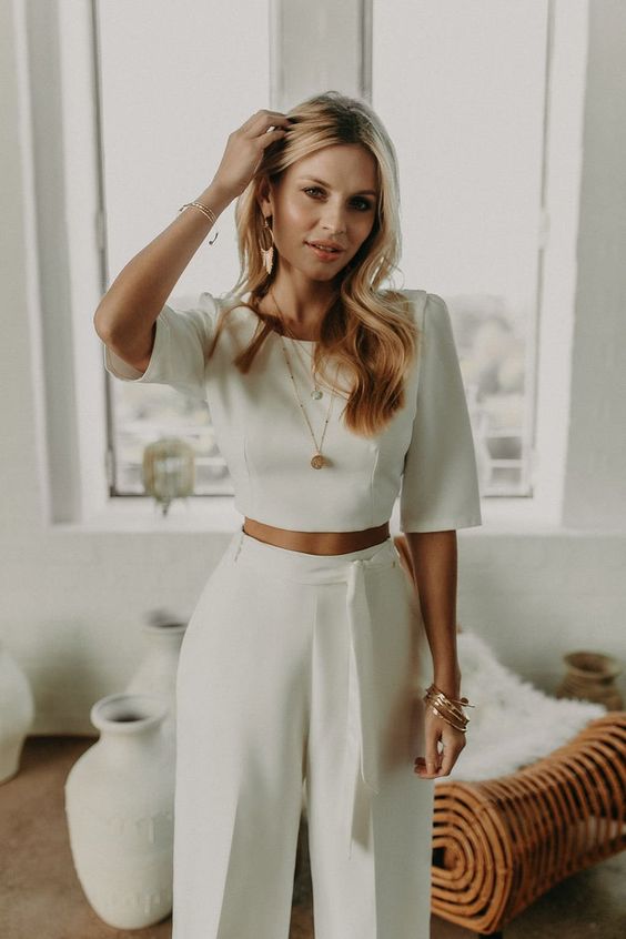 a minimalist bridal look with a plain crop top with short sleeves and high waisted pants with a sash, statement earrings and some more jewelry