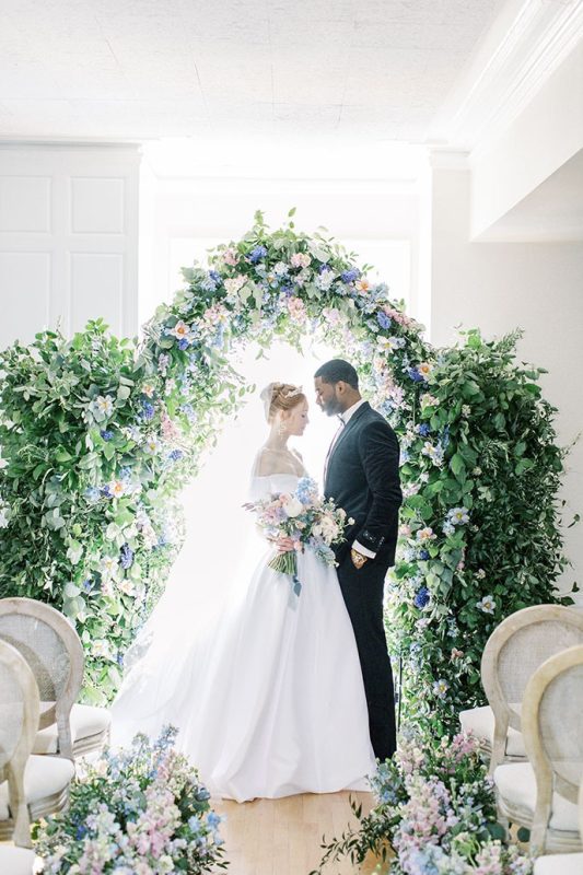 a beautiful lush wedding arch covered with lots of greenery and pastel-colored florals is a fabulous idea for a Bridgerton wedding.jpg