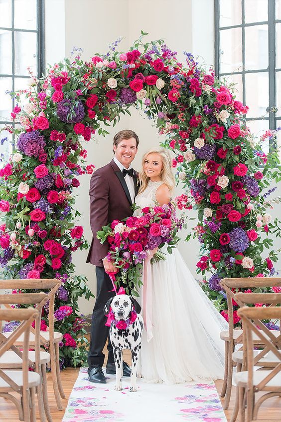 a super bold wedding arch done with fuchsia, red, purple, blush and pink blooms plus a matching wedding bouquet