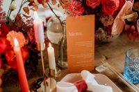 20 a bright and chic wedding tablescape with red, orange and pink blooms, an orange menu, colorful candles and a pink hex plate