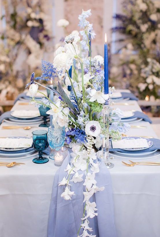 a lovely wedding tablescape with a periwinkle table runner, napkins and plates, bold blue candles and white and blue florals