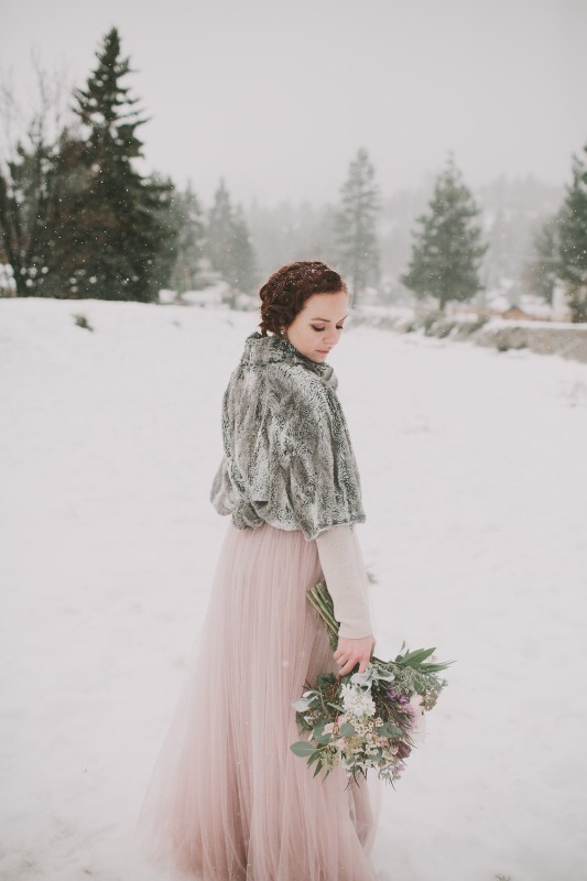 a winter bride rocking a pink A-line wedding dress with a layered skirt and long sleeves, a grey faux fur cover up for coziness