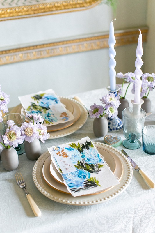 a delicate and chic wedding tablescape with pastel blooms, watercolor floral stationery, elegant porcelain and colored glasses