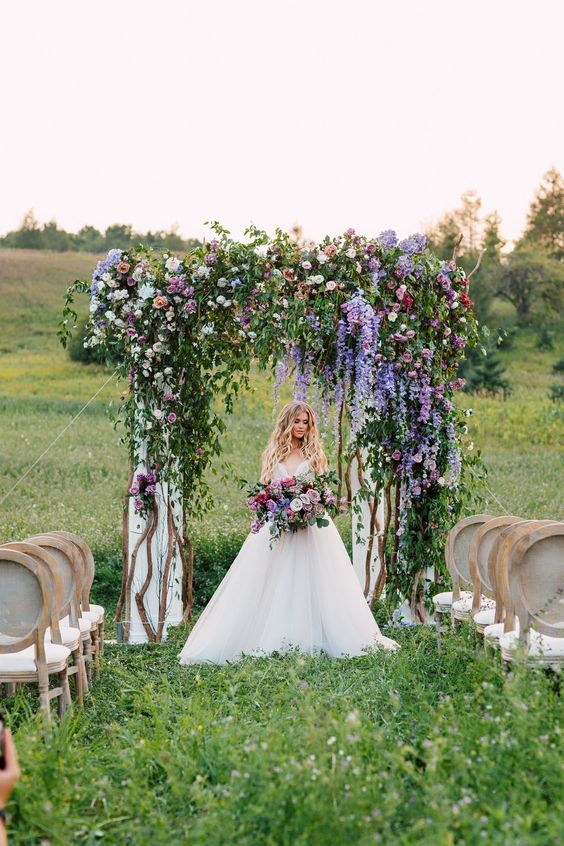 a lush wedding arch with lots of greenery, peachy, mauve, periwinkle blooms is a very bold and statement-like idea