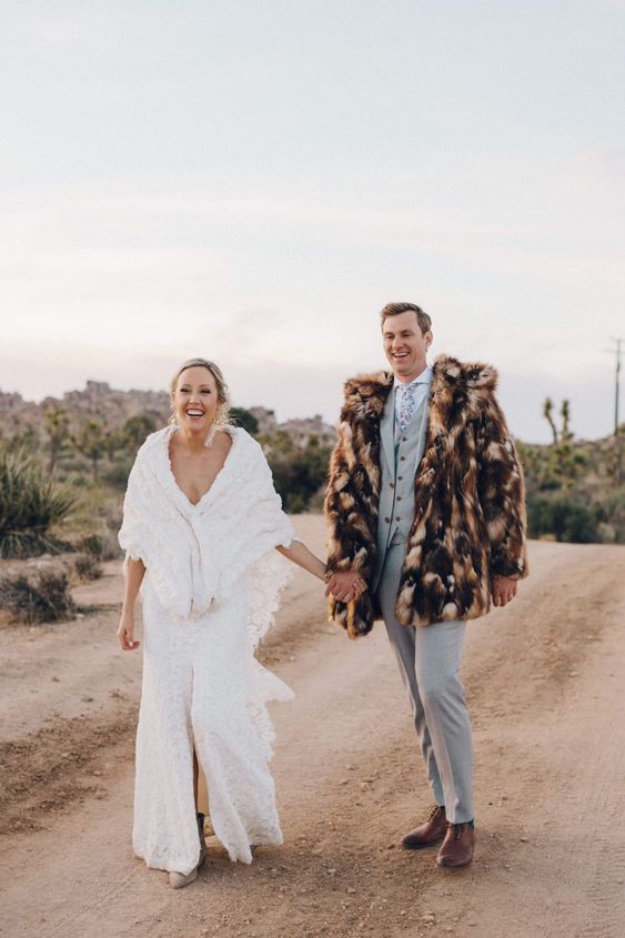 a groom wearing a brown spotted faux fur jacket to feel comfortable in the desert when it gets colder at night