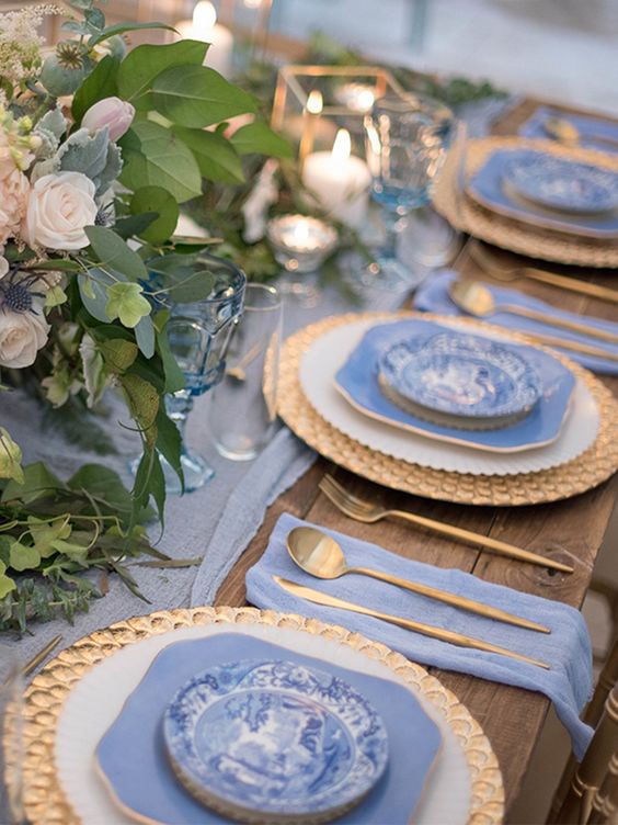 a pretty wedding tablescape with a periwinkle table runner, napkins, periwinkle plates, pastel blooms and candle lanterns