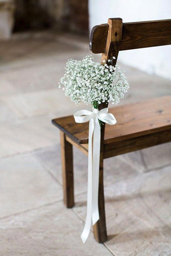 a wooden bench in the wedding aisle accented with a white bow with a baby's breath arrangement looks amazingly chic