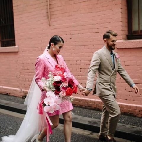 a short patterned pink blazer wedding dress, a long white veil, statement pearl earrings and white shoes plus a whimsy bouquet