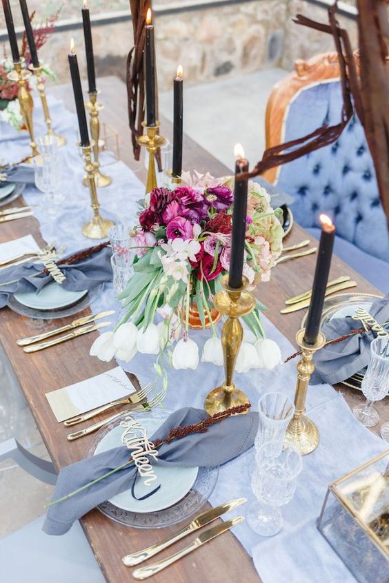 a sophisticated periwinkle wedding tablescape with a peri table runner, napkins, a bold floral centerpiece, black candles and gold touches
