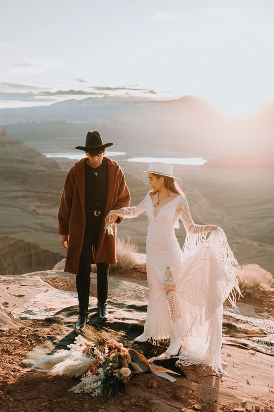 a unique boho winter groom's look with a black shirt and trousers, black boots and a hat plus a brown faux fur coat for comfort