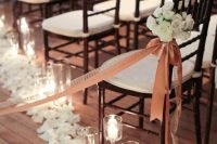 27 a dark and white wedding chair in the aisle accented with an orange ribbon and a bow plus a white floral arrangement and candles and petals on the floor