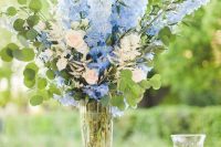 28 a tall wedding centerpiece of a clear vase with blue and periwinkle blooms plus greenery and candles is a color statement