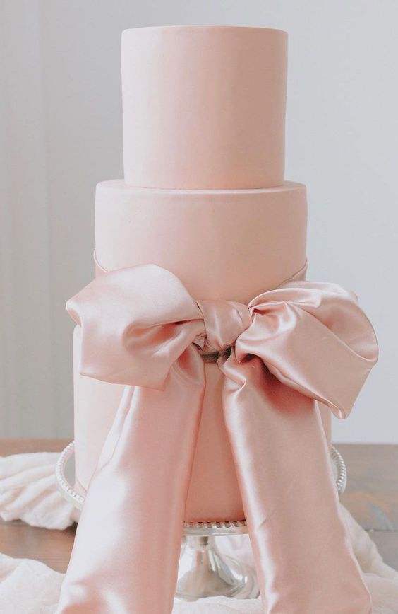 a large pink wedding cake with a large pink silk bow of ribbon is a gorgeous idea for a refined wedding done with pastel colors