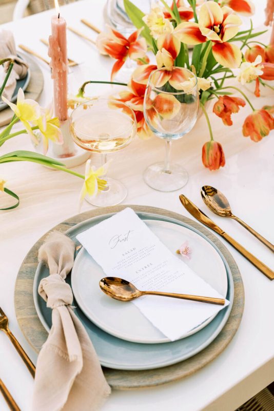 a lovely Bridgerton-inspired wedding tablescape with bold tulips, pastel candles, printed chargers and blue plates and elegant cutlery