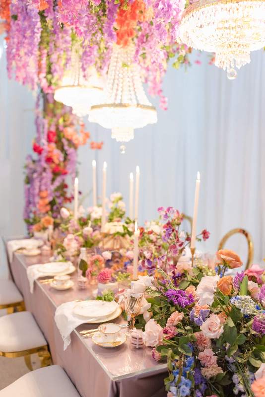 a jaw-dropping Bridgerton wedding tablescape with super lush pastel and bright florals on the table and over it, with tall and thin candles and delicate porcelain