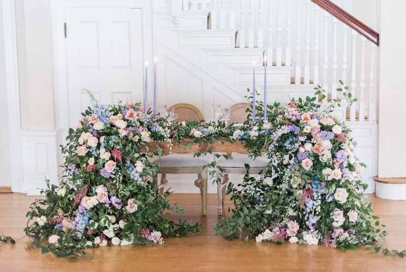 A gorgeous sweetheart table with lilac candles and super lush florals and greenery descending to the floor is wow
