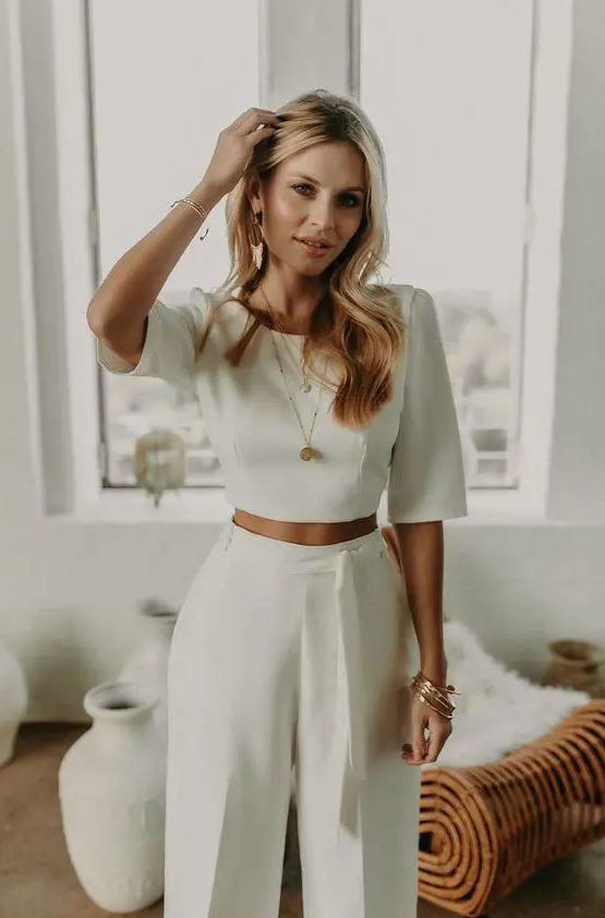 A minimalist bridal look with a plain crop top with short sleeves and high waisted pants with a sash, statement earrings and some more jewelry