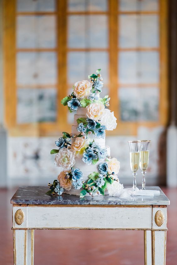 a beautiful wedding cake decorated with natural and sugar blooms in peachy and blue plus greenery for a Bridgerton wedding