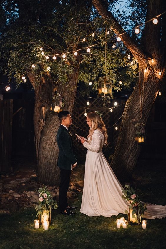an intimate backyard garden evening wedding ceremony under living trees, with lots of lights and candles