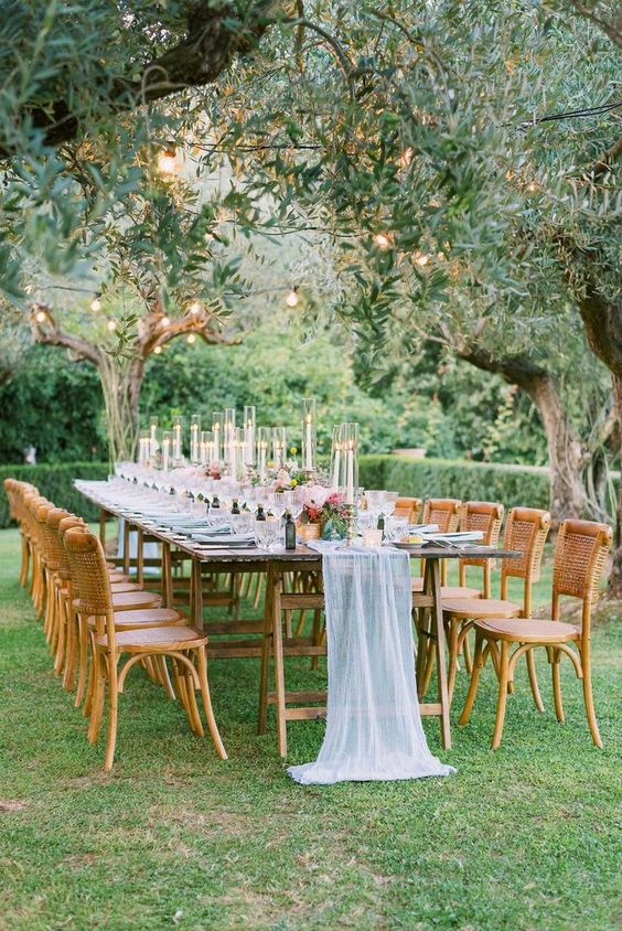 a beautiful garden wedding reception space with string lights, trestle tables, woven chairs and pastel linens