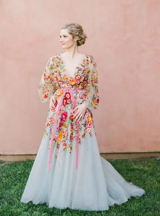 a blush A-line wedding dress with colorful floral embroidery, a plunging neckline, long sleeves and a pink sash for a garden wedding