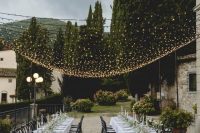 39 a beautiful and chic al fresco wedding reception with greenery runners and candles, with refined chairs and a warm light canopy