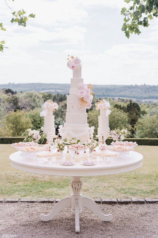 a jaw-dropping wedding dessert table with an assortment of neutral wedding cakes topped with pastel and gilded blooms, macarons, souffle and other sweets
