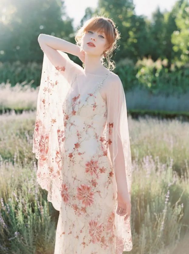 a delicate wedding dress in neutral shades with pink floral embroidery all over the dress and with a neutral underdress