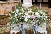 41 a refined console table decorated with super lush and pretty florals, with blue thin and tall candles, a white textural wedding cake with pasinted blooms