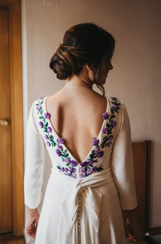 a wedding dress featuring purple and lilac embroidered flowers and leaves, a cutout back on buttons and a long train