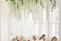 50 a delicate wedding reception with lush white flowers and greenery hanging down over the table and white and pink blooms on the table