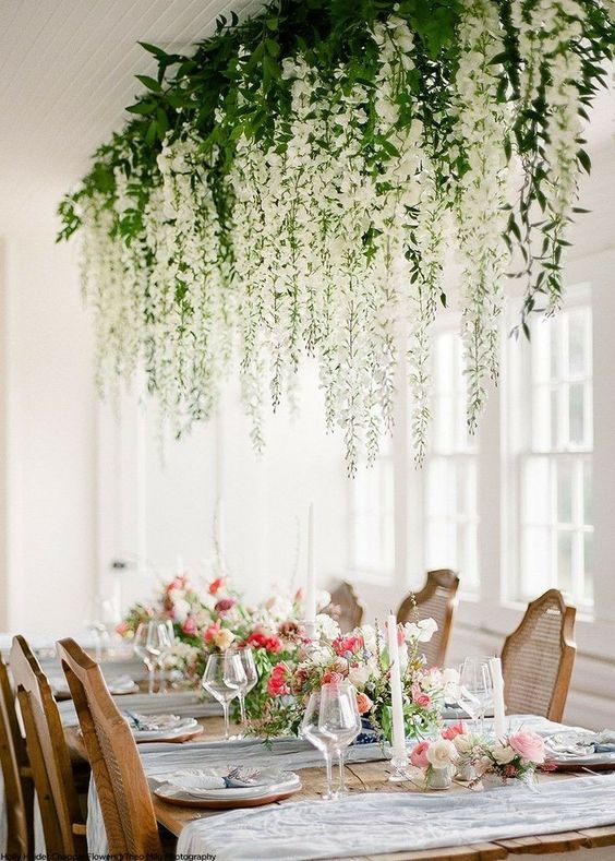 a delicate wedding reception with lush white flowers and greenery hanging down over the table and white and pink blooms on the table